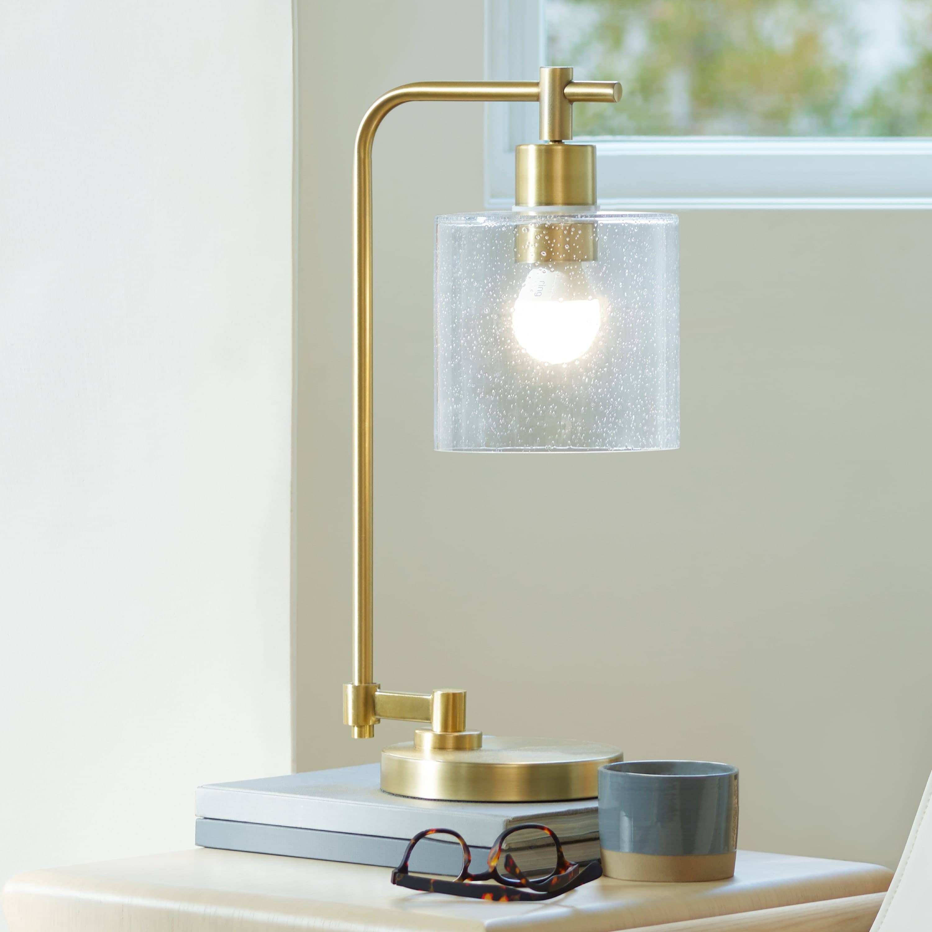 Smart Lighting A19 Smart LED Bulb - Indoors on an end table, a modern lamp with an A19 Smart LED light bulb shines through a clear lampshade.